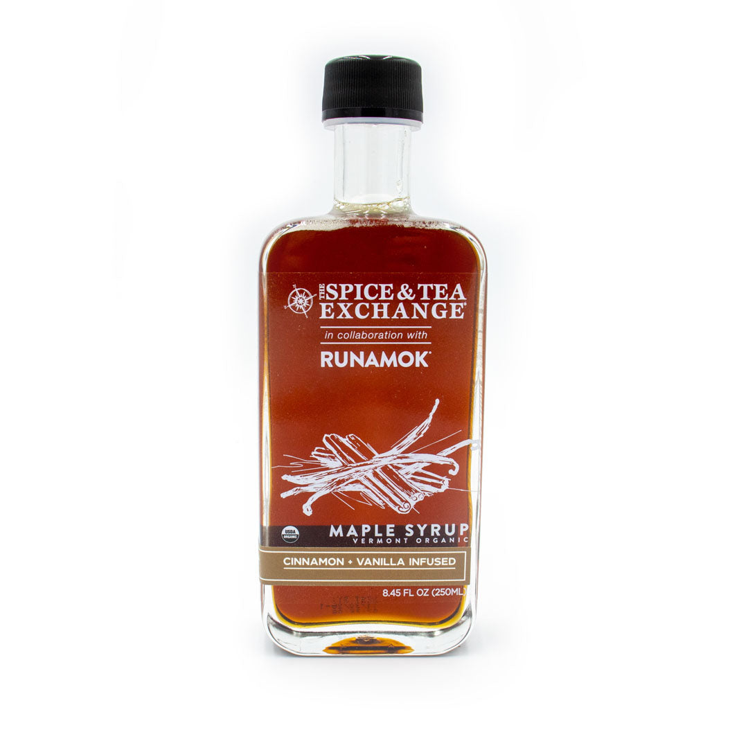 A clear glass bottle labeled Spice & Tea Exchange x Runamok holds Organic Cinnamon Vanilla Maple Syrup, featuring drawings of cinnamon sticks and vanilla pods that highlight its unique flavor.
